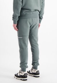 Pantalons de jogging en coton gris avec une coupe slim, des poignets élastiques et un détail de logo sur la cuisse gauche, associés à des baskets noires à motifs.