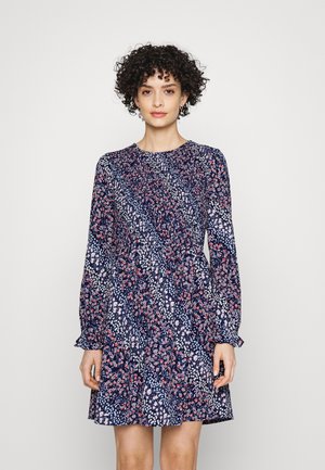 Vestido azul marinho com estampado floral em branco e vermelho. Apresenta mangas longas e decote redondo, feito de um tecido leve com um design fluido.