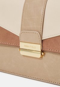 Borsa strutturata beige e marrone chiaro con chiusura in metallo dorato, caratterizzata da materiale texturizzato e dettagli cuciti. Etichetta del marchio visibile.