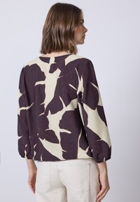 Blouse à manches courtes en crème avec un grand motif de feuilles bordeaux. Tissu léger, coupe décontractée, encolure ronde et manches froncées.