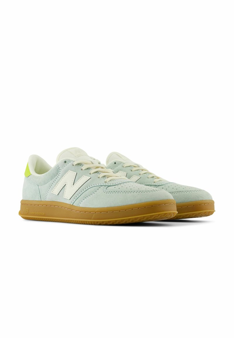 Zapatillas de ante verde claro con un logo blanco, cordones crema y una suela de goma. Presentan una superficie texturizada y perforaciones en la puntera.