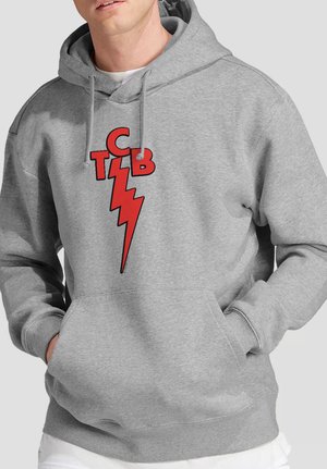 Mann trägt einen grauen Kapuzenpullover mit einer Vordertasche und einem roten Blitz-Design, das von den Buchstaben C, T, B auf der Brust gekrönt wird.