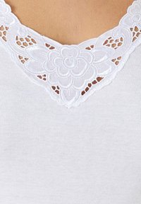 Top bianco senza maniche con un dettaglio in pizzo floreale sullo scollo. Il tessuto è a coste e morbido, con delicate rifiniture sul dettaglio in pizzo.