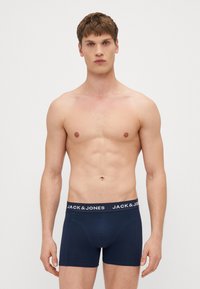 Marineblaue Boxer-Shorts aus Baumwolle mit enganliegendem Schnitt, ausgestattet mit einem elastischen, gebrandeten Taillenbund. Das Modell ist oberkörperfrei und zeigt die Shorts.