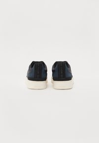 Tumedad sneakersid on tekstuuriga, siledal pinnal, valgete talladega, tagaküljel on bränding ja madala sääre disain.