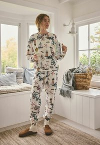 Pohodlný pyžamový set v krémové barvě s barevnými námořnickými motivy; disponující dlouhými rukávy, elastickými manžetami a kalhotami ve stejné barvě. Hnědé texturované papuče.