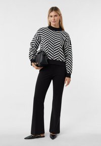 Sweter w czarno-białe paski z okrągłym dekoltem, w połączeniu z czarnymi rozkloszowanymi spodniami i małą czarną torebką typu bucket. Czarne baleriny z noskiem w szpic.