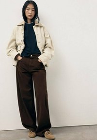 Cream jacket, dark shirt, brown wide-leg pants, and light brown shoes. Smooth fabric, relaxed fit, and minimalistic design.