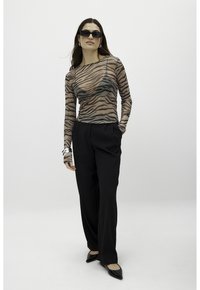 Sheer long-sleeve top with a tiger stripe pattern in neutral tones, paired with tailored black trousers and pointed-toe flats.