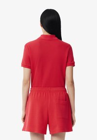 Röd overall i mjukt tyg, med polo-krage, korta ärmar, elastisk midja och en bakficka. Enkel och modern design.