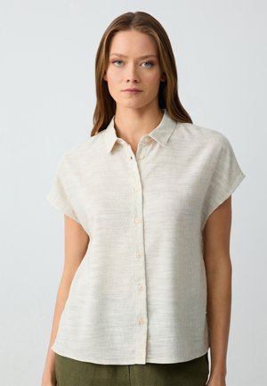 Camicia corta beige chiaro realizzata in tessuto testurizzato con colletto e chiusura a bottone, caratterizzata da sottili strisce orizzontali.