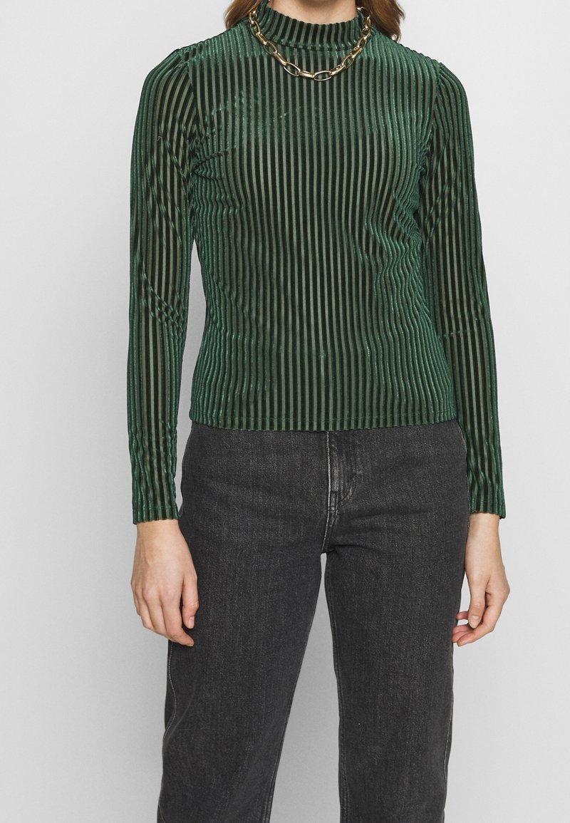 Grünes, geripptes Langarmshirt aus glänzendem Material mit hohem Kragen. Verfügt über vertikale Streifen und eine goldene Kettenzierkette.