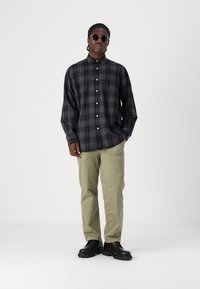 Camisa de cuadros en negro y gris, con cuello y mangas largas, combinada con pantalones cargo en color caqui claro y zapatos negros.