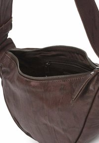 Bolso de hombro de cuero marrón con forma curva. Cuenta con un cierre de cremallera y un pequeño bolsillo interior. Textura suave con un ligero brillo.