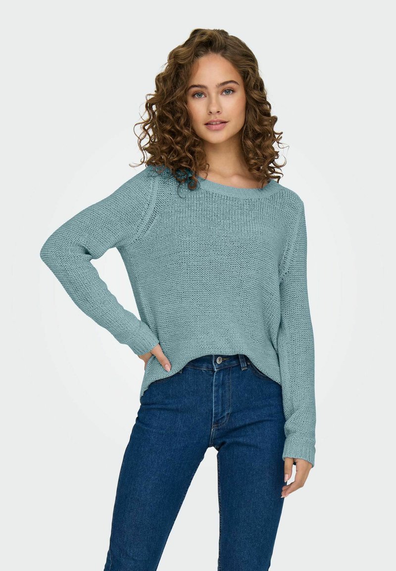 Maglione azzurro chiaro lavorato a maglia con scollatura ampia e maniche lunghe, abbinato a jeans scuri a vita alta. Tessuto testurizzato con vestibilità comoda.
