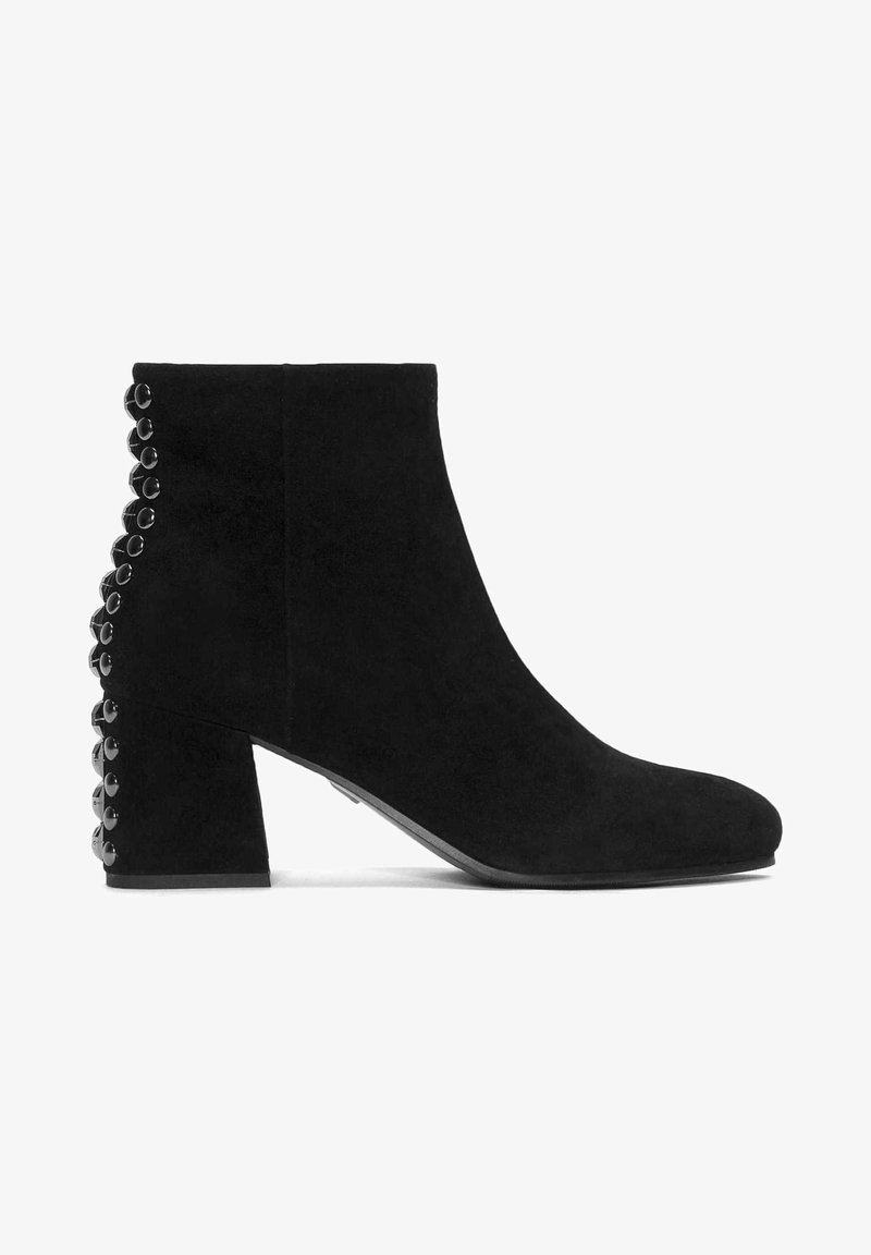 Stivale alla caviglia in suede nero con tacco a blocco e accenti circolari neri lungo il lato, texture liscia e design della punta arrotondata.