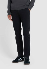 Zwarte tapered broek van lichtgewicht stof, met zijzakken, gecombineerd met zwarte suède sneakers met witte strepen en veters.