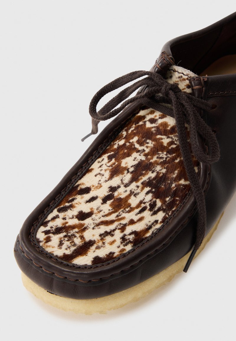 Chaussure en cuir avec un corps marron, un panneau en fourrure tachetée décoratif, un bout rond et des lacets marron. Semelle beige douce avec des détails de couture.