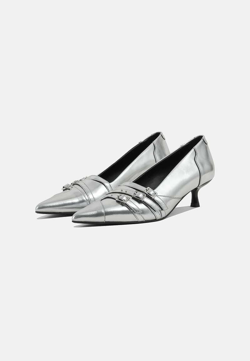 Scarpe con tacco a punta color argento metallizzato con due cinturini decorativi dotati di fibbie, tacco basso e superficie liscia e riflettente.