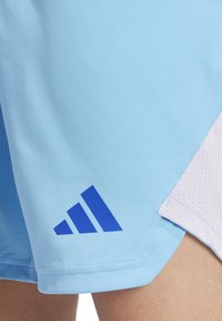 Lichtblauwe sportshorts van een gladde stof, met een blauw Adidas-logo aan de linkerkant en een witte textuurpaneel aan de rechterkant.