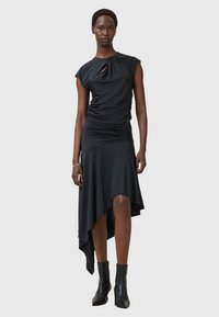 Schwarzes Kleid mit tailliertem Oberteil und asymmetrischem Saum. Hergestellt aus glattem Stoff, mit einem gedrehten Knoten-Detail am Ausschnitt.