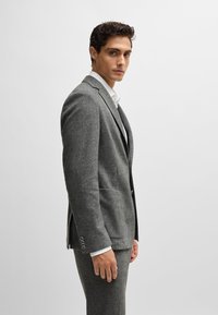 Gray wool suit with a tailored fit. Features a two-button blazer, notch lapels, and side pockets. Accompanied by a white shirt under the jacket.