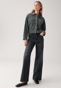 Grijze corduroy cropped jack met grote frontzakken en knopen, gecombineerd met hoge taille, wijde zwarte jeans en zwarte ballerina's.