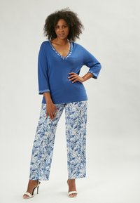 Top in maglia blu con scollo a V e bordatura decorata, abbinato a pantaloni larghi con stampa di foglie blu su sfondo bianco.