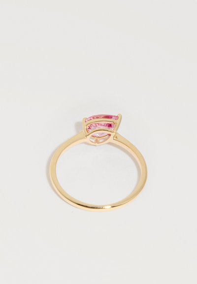 Λεπτό χρυσό δαχτυλίδι με ένα ροζ μαρκιζέ κομμένο πολύτιμο λίθο τοποθετημένο οριζόντια σε μια μίνιμαλ βάση σε λευκό φόντο.