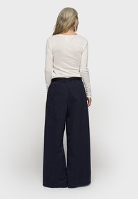 Marineblauwe wijde broek met een relaxed fit, elastische tailleband en zwarte riem, gecombineerd met een lichtbeige top met lange mouwen. Eenvoudig ontwerp zonder patronen.