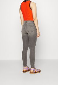 Jeans ajustados grises y una camiseta sin mangas ajustada de canalé naranja, combinados con sandalias moradas con tiras. Tela suave y diseño de cintura alta visibles.