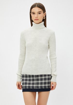 Pull à col roulé côtelé gris clair à manches longues, associé à une mini-jupe à carreaux bleu marine et crème avec un bord inférieur bleu marine uni.