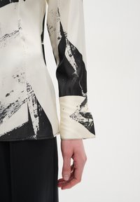 Long-sleeve blouse in lightweight fabric, cream with bold black abstract patterns; features a smooth texture and tailored cuffs.