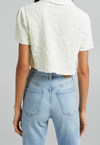 Cropped white textured shirt with a collar, paired with high-waisted light blue denim jeans featuring back pockets and visible stitching.