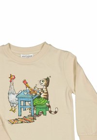 Katt i gröna byxor som äter vid ett blått bord med två kycklingar, en som sitter och en som står, på en krämfärgad långärmad tröja med en färgglad matta.