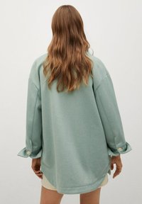 Camicia oversize verde menta realizzata in un tessuto morbido, con maniche lunghe con dettagli a bottoni e orlo curvato per un fit rilassato.