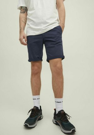 Marina shorts, uppvikta benslut, bomullsmaterial. I kombination med svarta och grå sneakers, randiga vita strumpor. Enkel, avslappnad design.