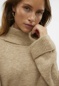 Maglione lavorato a maglia beige con colletto alto, caratterizzato da una finitura testurizzata e maniche larghe a costine. Materiale morbido con sottili variazioni di colore.