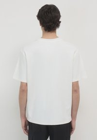 T-shirt bianco a maniche corte con orlo dritto e scollo rotondo, realizzato in un tessuto morbido, mostrato di spalle. Nessun motivo o logo visibile.