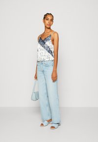 Camiseta blanca sin mangas con ribete de encaje azul marino, pantalones vaqueros de pierna ancha azules, sandalias azul claro y un pequeño bolso azul. Tejido suave, corte relajado.