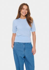 Light blue knitted short-sleeve sweater with a textured zigzag pattern and ribbed hem. Paired with loose-fitting blue denim trousers.