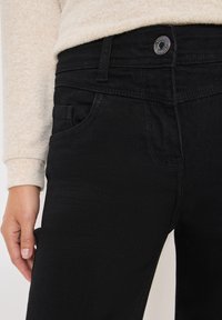 Czarne dżinsy wykonane z denimu, o slim fit, widoczna przednia kieszeń oraz metalowe zapięcie. Teksturowana powierzchnia i przyszyte detale.