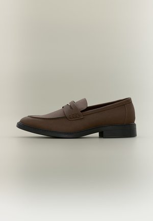 Brun læder slip-on loafer med sort sål og lav hæl, vist fra højre side på en neutral baggrund.