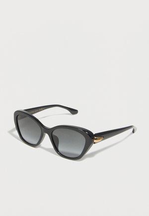 Schwarze Cateye-Sonnenbrille mit dunklen Verlaufszähnen und goldenen Akzenten an den Bügeln, gezeigt auf weißem Hintergrund.