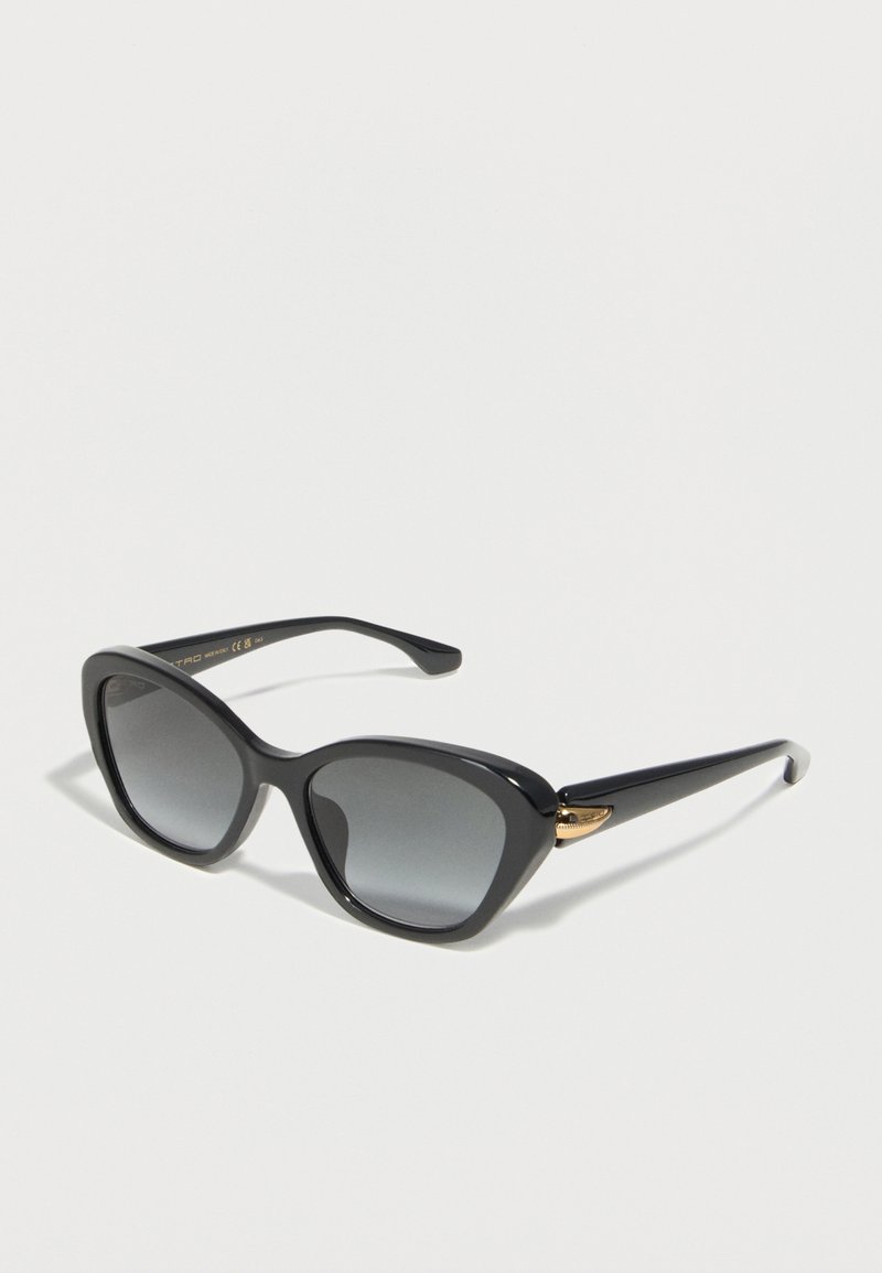 Lunettes de soleil œil de chat noires avec des verres dégradés foncés et des accents dorés sur les branches, présentées sur un fond blanc.