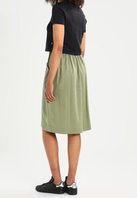 Czarna skrócona koszulka, zielona spódnica do kolan z elastycznym pasem, noszona z czarnymi trampkami z srebrnymi akcentami. Gładki, swobodny styl.