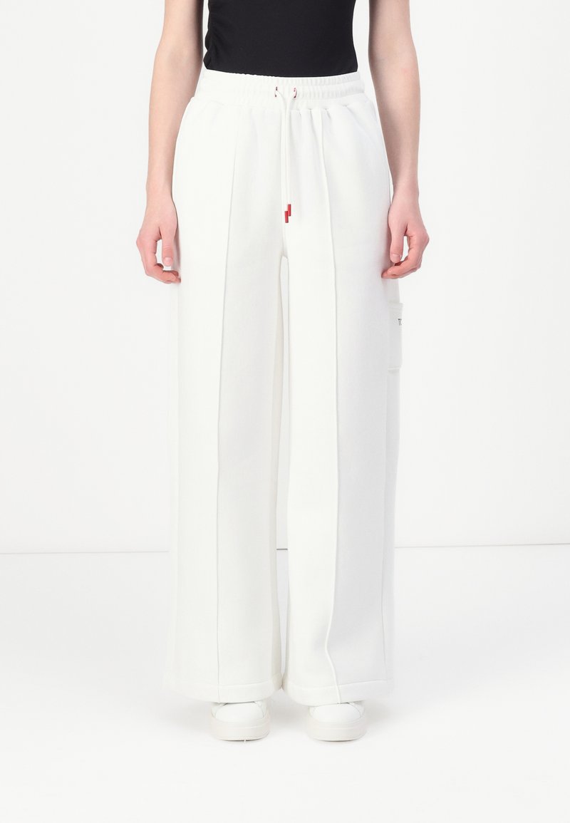 Pantalones de chándal anchos y blancos con una cintura elástica, que presentan un cordón delantero y un bolsillo lateral. Tejido suave y estructurado con acentos mínimos.