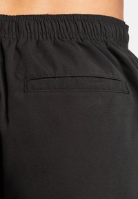 Black athletic shorts featuring an elastic waistband and a small back pocket with a rectangular shape, made from a smooth, lightweight fabric.