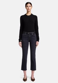 Un pull noir ajusté, un jean cropped en denim foncé avec un ourlet brut, et des ballerines brunes à imprimé animal à bout pointu. Des accents de bijoux en argent minimalistes.
