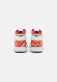 Vysoké tenisky z bílé kůže, s červeným vnitřkem, zlatými akcenty a texturovaným červeným a zlatým vzorem na zadní patě. Průhledná podrážka.